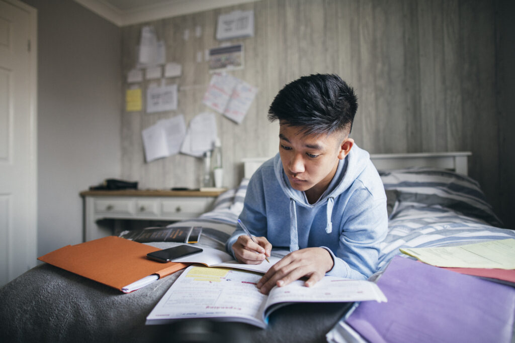 Teenage boy lying on his bed while concentrating on homework for his exams.